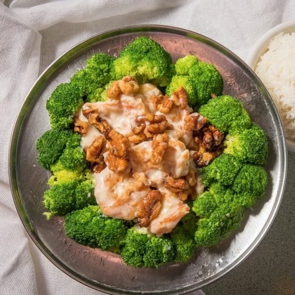 Honey walnut shrimp with creamy sauce and broccoli florets on a silver platter, with a side of rice.